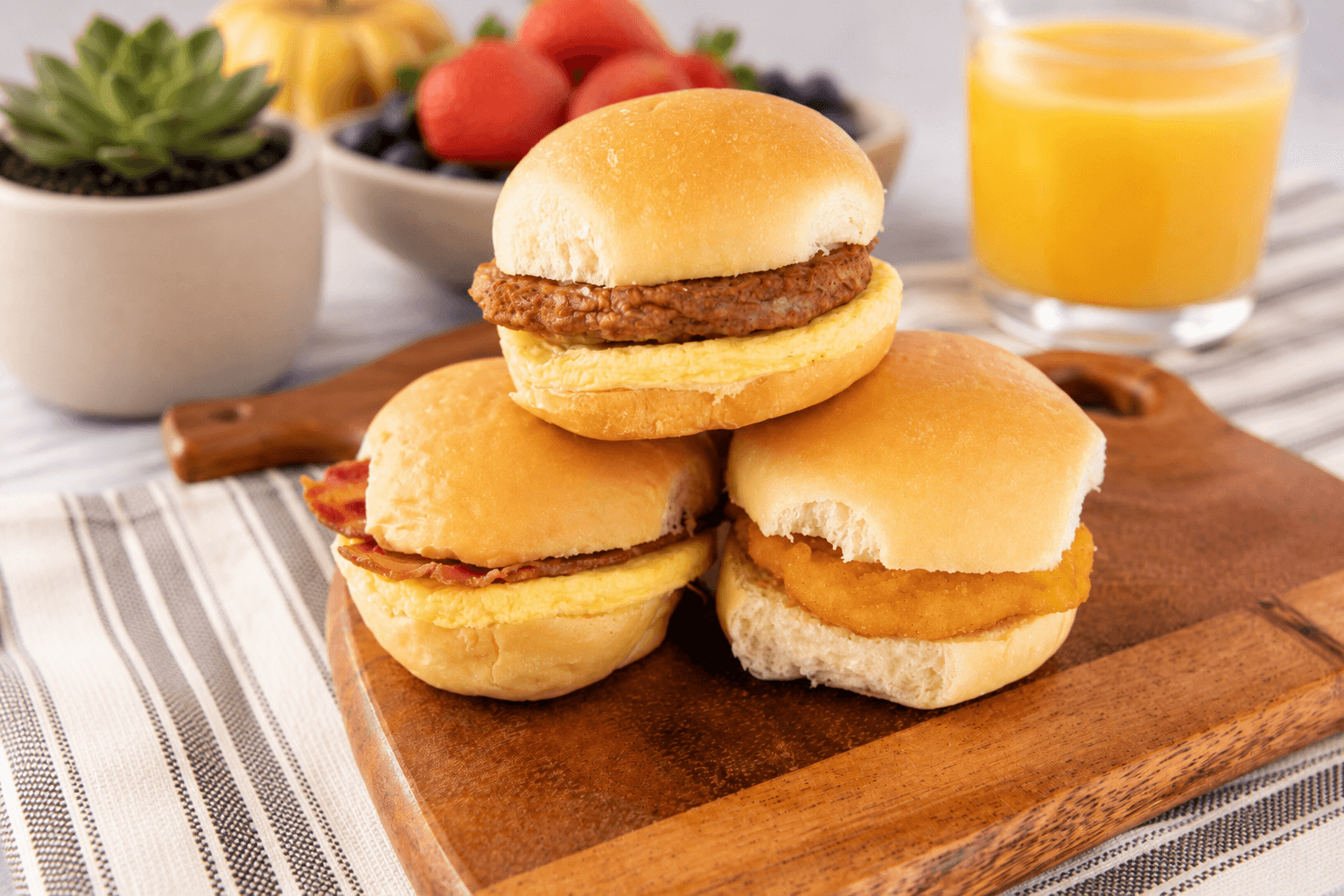 Breakfast slider sandwiches stacked on a wooden board