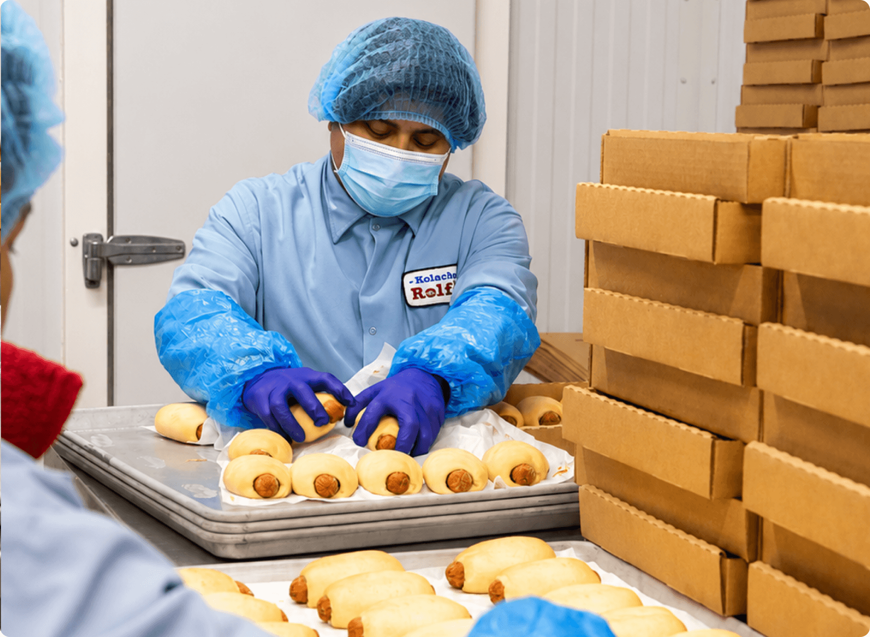 A worker in food-safety gear packing kolaches in the production facility